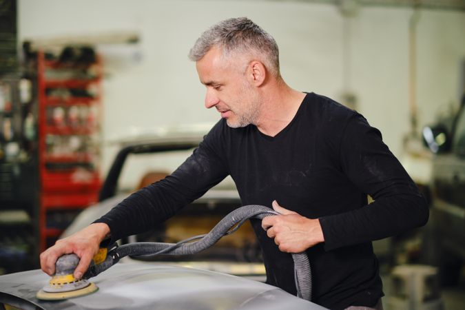 Mechanic grinding paint from car detail