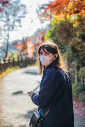 Female tourist with facemask standing near autumn trees in Tokyo, Japan