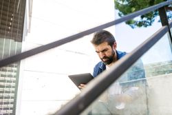 Serious man sitting on stairs checking tablet outdoors