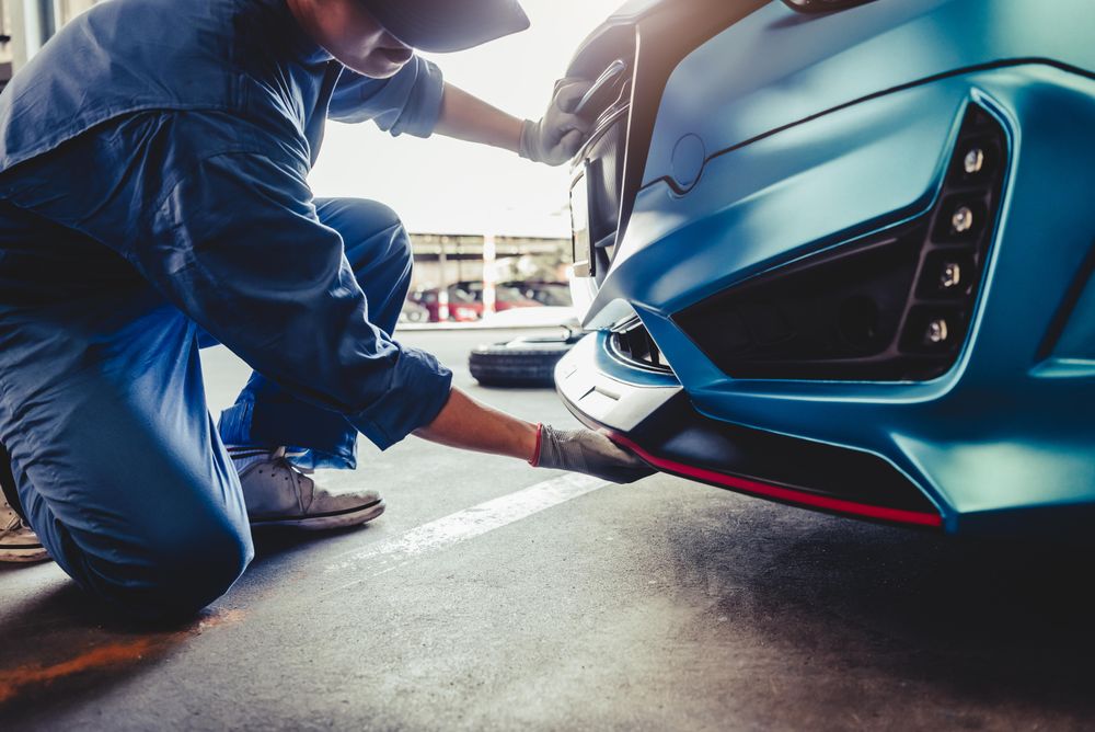 Car mechanic crushing next to car checking bumper