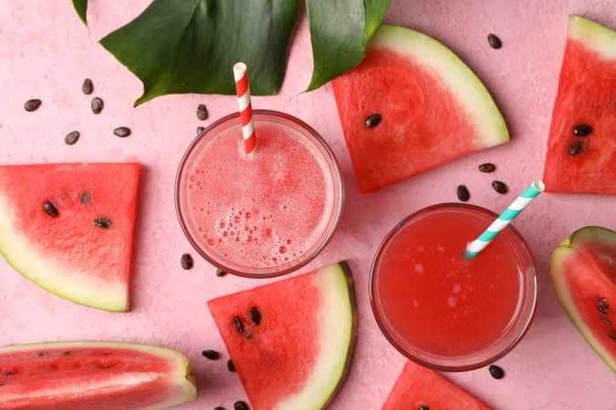 Composition with glass of watermelon juice and slices on pink table