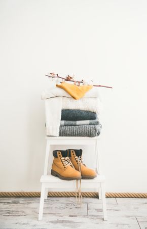 Pile of folded sweaters on light background with yellow boots, dried cotton, vertical composition
