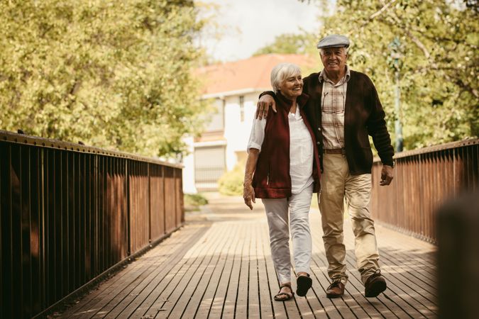 Full length of happy older couple walking through a park on a bridge