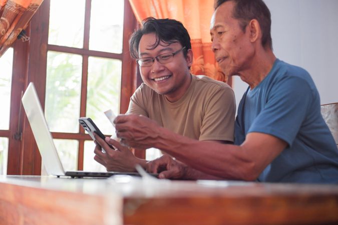 Happy adult son and mature father pay online using laptop and credit card