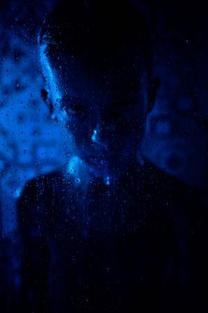 Displeased boy behind glass wall with water drops