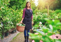 Pensive woman pictured in a greenhouse holding a basket of flowers