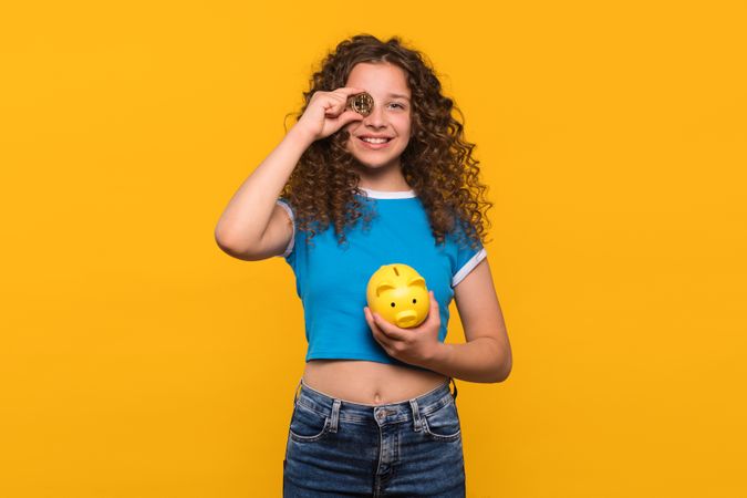 Girl smiling and holding Bitcoin and piggy bank