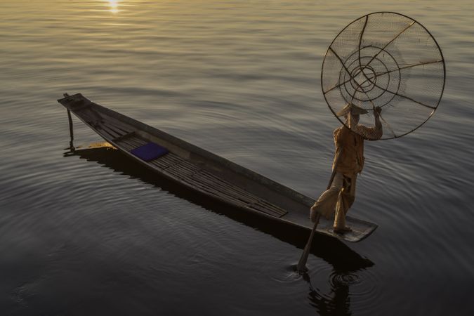 Fisherman standing on boat throwing the fishing net into water in Myanmar