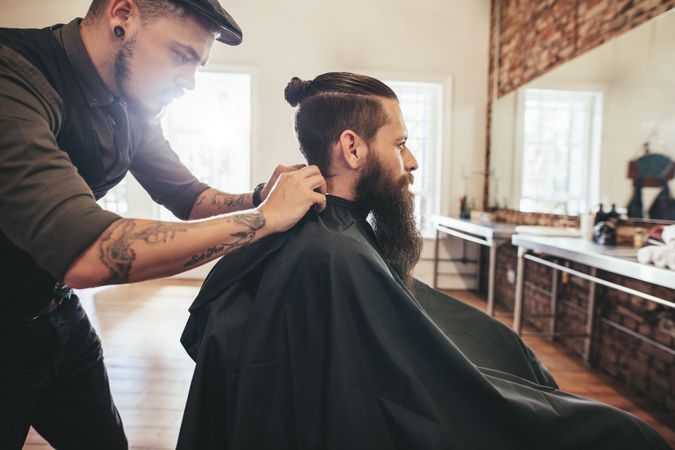 Barber buttoning cape on customers neck before haircut