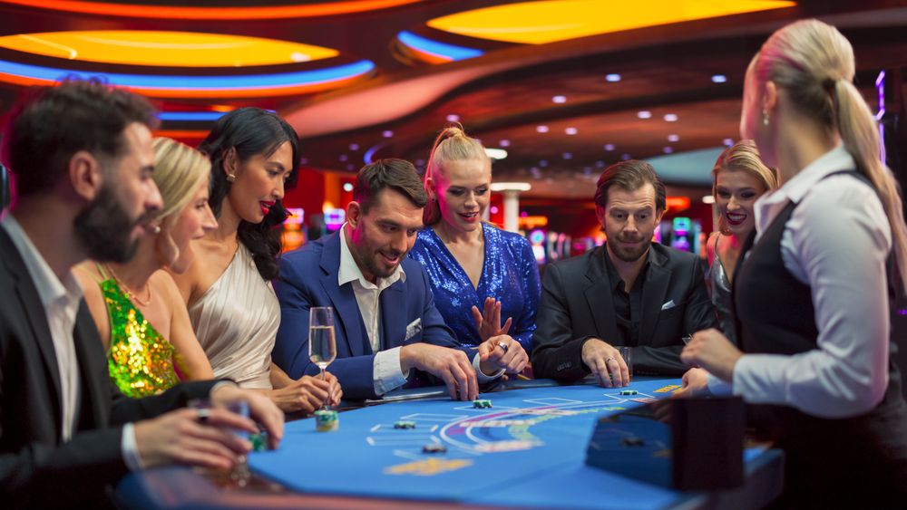 Group of Casino Goers Enjoying Time in a Modern Casino, Friends Placing Blackjack Bets, Professional Female Croupier Deals Cards.