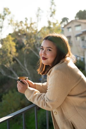 Young multiracial woman smiling outside holding coffee cup on patio