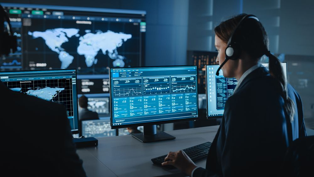 Analyst Monitors Global Data on Multiple Screens in Dark Control Room.