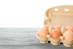Brown chicken eggs in carton box on wooden table isolated on light background, space for text