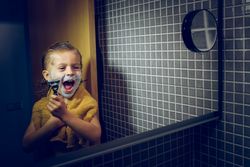 Happy boy with shaving razor in bathroom