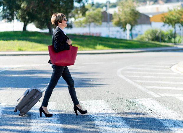 Woman in heels walking across cross walk with luggage