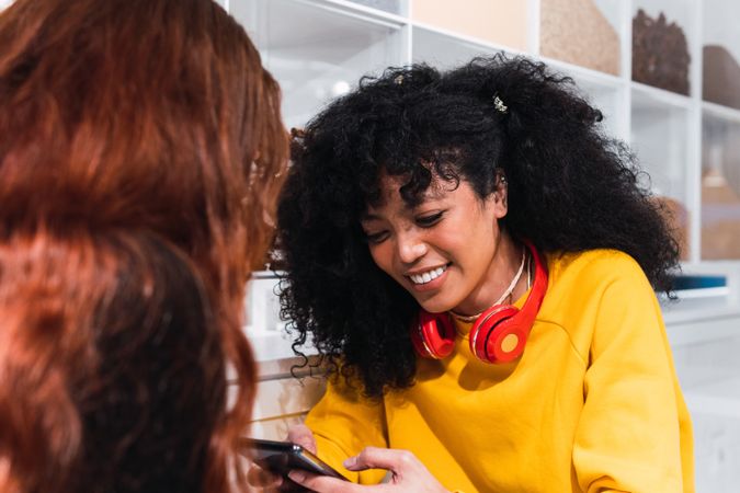Positive multiethnic female friends using smartphones and laughing in cafe