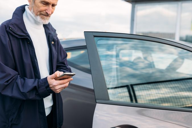 Mature man opening a door of his car while looking at phone