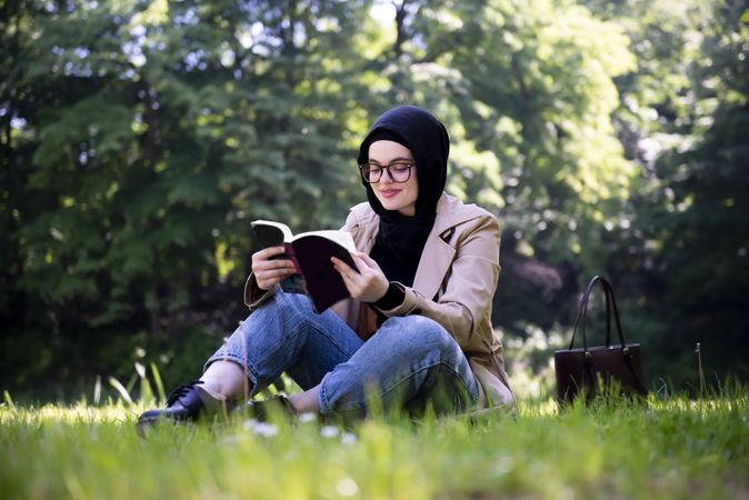 Woman sitting in grassy forest with book