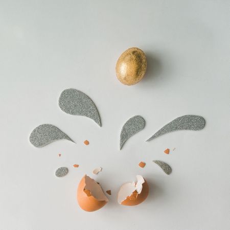 Golden Easter egg with silver and golden glittering splashes on light background