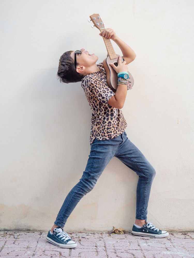 Excited kid raising hands up with ukulele