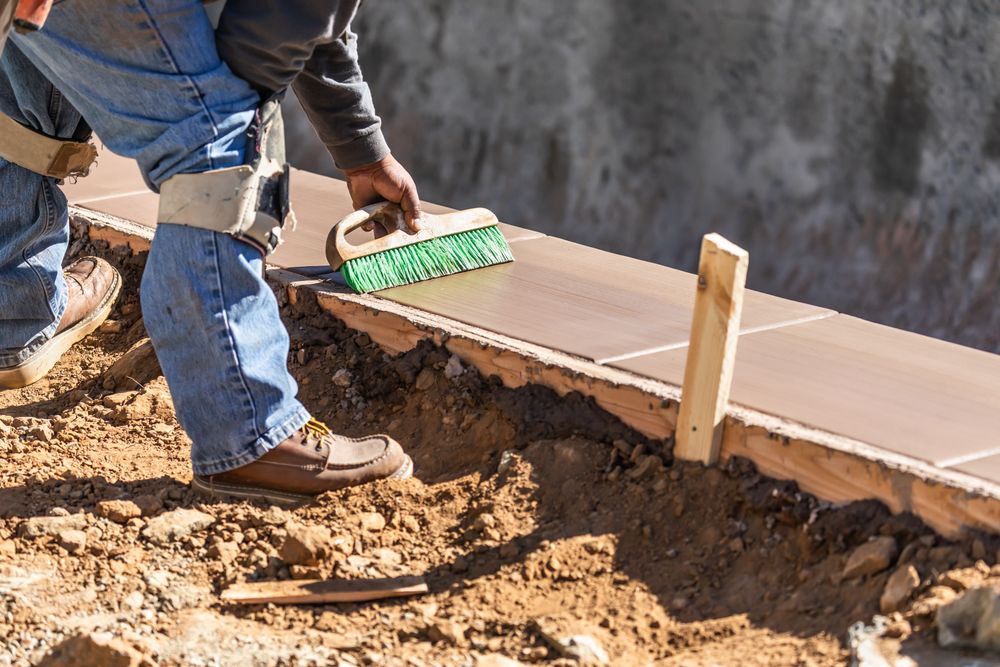 Construction Worker Using Brush On Wet Cement Forming Coping Around New Pool