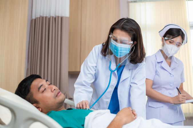 Female doctor using stethoscope examine to sick man with nurse