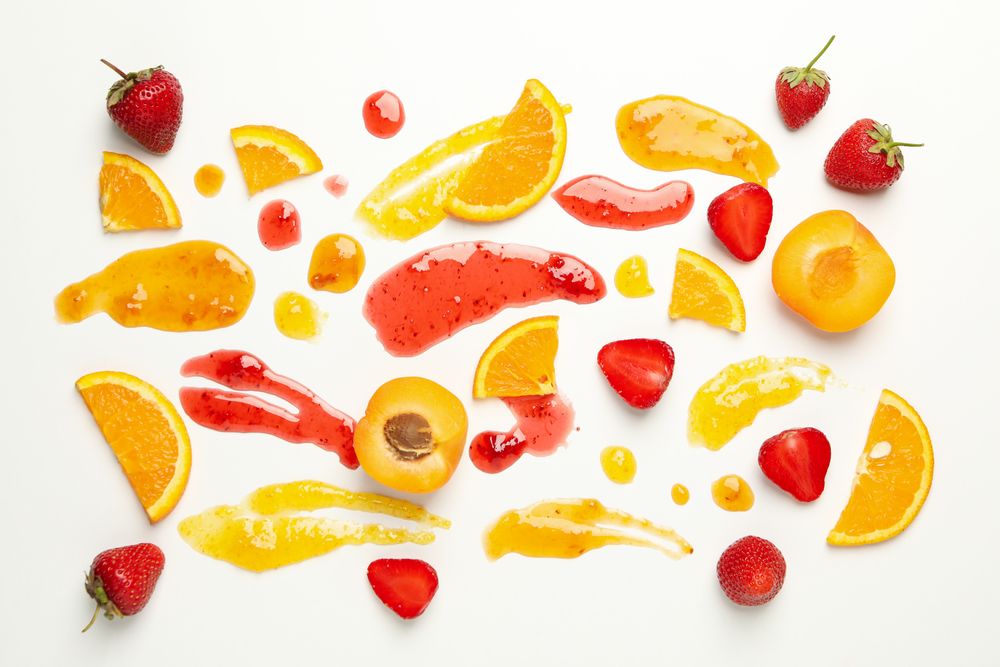 Apricot, strawberry, orange and jams on plain background