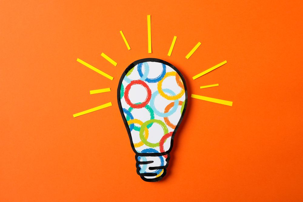 Light bulb with multicolored circles on orange background, space for text