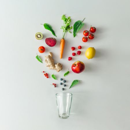 Neatly arranged fruits, vegetables and herbs and glass on bright table background