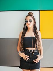 Charming teenage girl with dreadlocks in sunglasses nearby colorful wall