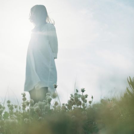 Woman in light dress standing on light flower field under clear sky