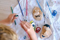 Crop child painting rocks with watercolors