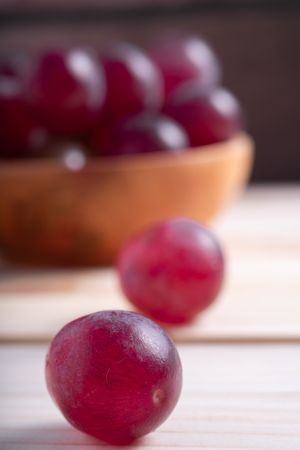 A bowl of red grapes sits on a wooden table