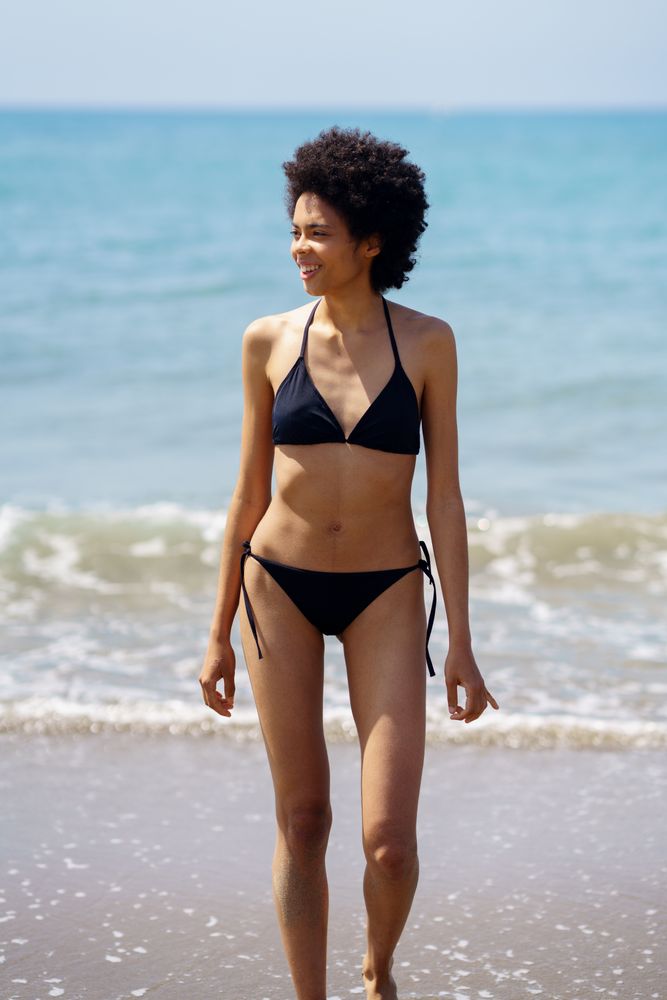 Smiling woman walking on shore in bikini looking around