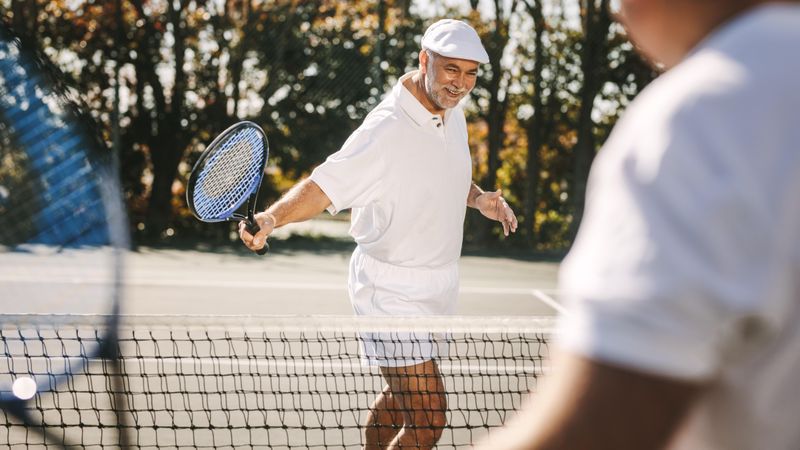 Smiling older man in tennis wear playing tennis with friend