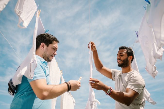Multiracial men hanging clothes in bright day