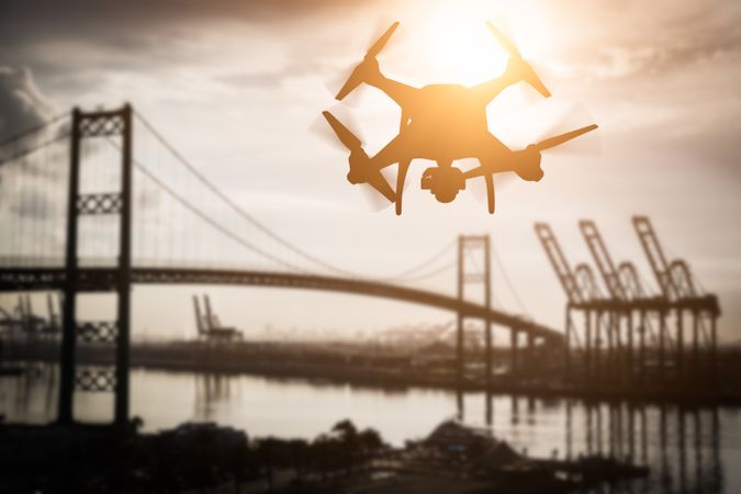 Silhouette of Unmanned Aircraft System (UAV) Quadcopter Drone In The Air Over Shipping Port.