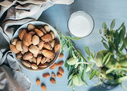 Glass of almond milk next to plate of almonds in shells on kitchen table