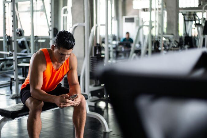 Serious male using mobile phone in sport club before workout exercise