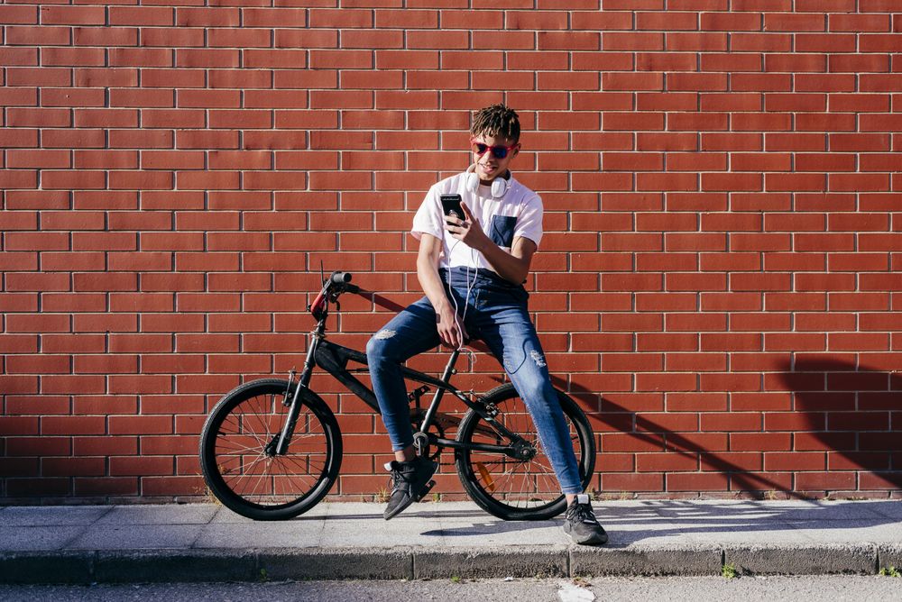 Young happy Black male browsing smartphone on bike