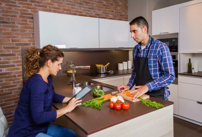 Woman checking digital tablet as her and her partner prepare dinner