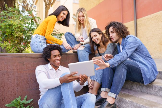 Multi-ethnic friends gathered around a digital tablet outside