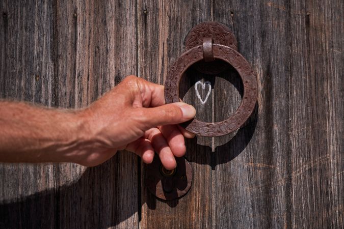 Crop person touching metal knocker on old wooden door