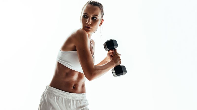 Sportswoman exercising with dumbbells over light background