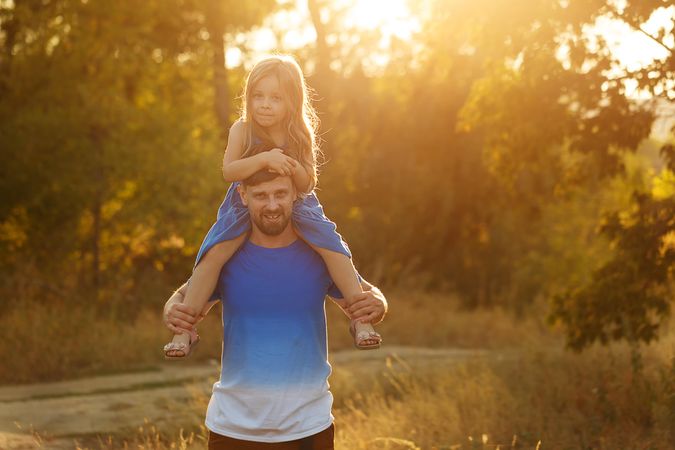 Dad with daughter on shoulders dressed in blue walking along forest road
