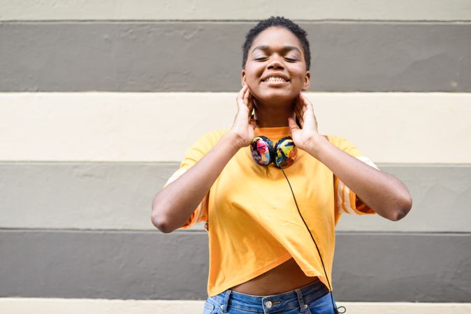 Smiling Black woman with headphones in front of grey striped wall