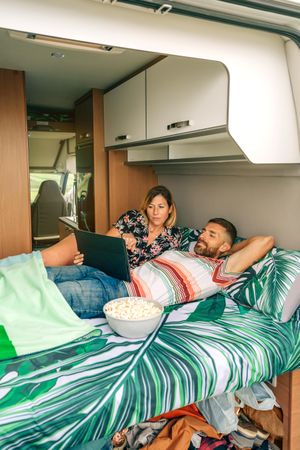 Male and female relaxing on bed in motorhome with popcorn, vertical