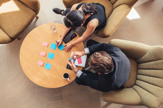 Top view of businessman and businesswoman discussing over adhesive notes on table in office lobby