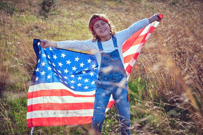 Positive boy having fun with USA flag on meadow