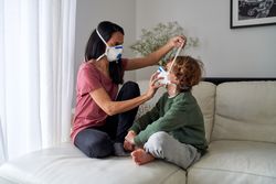 Son and mom wearing protective masks together on couch